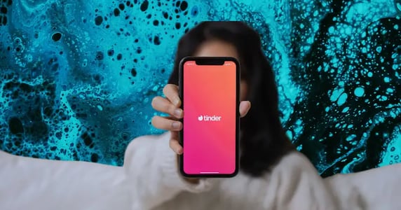 A woman holds a smartphone with the Tinder app’s logo up to the camera